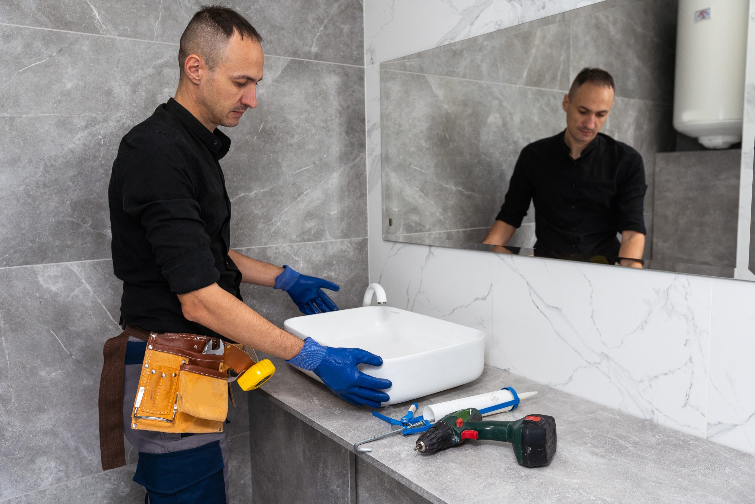 professional plumber, male worker in uniform installing sink and water pipe in new apartment