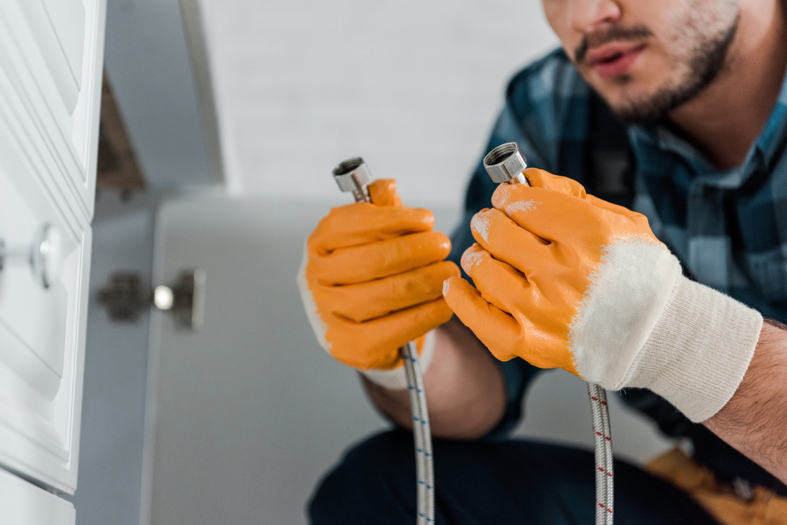 selective focus of handyman holding metal hose near kitchen cabinet