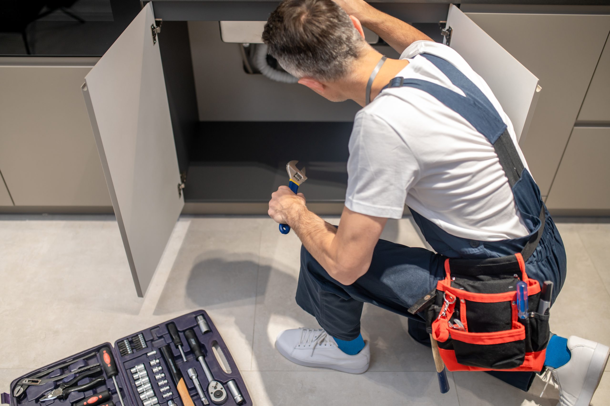 top view of man with wrench crouched near sink