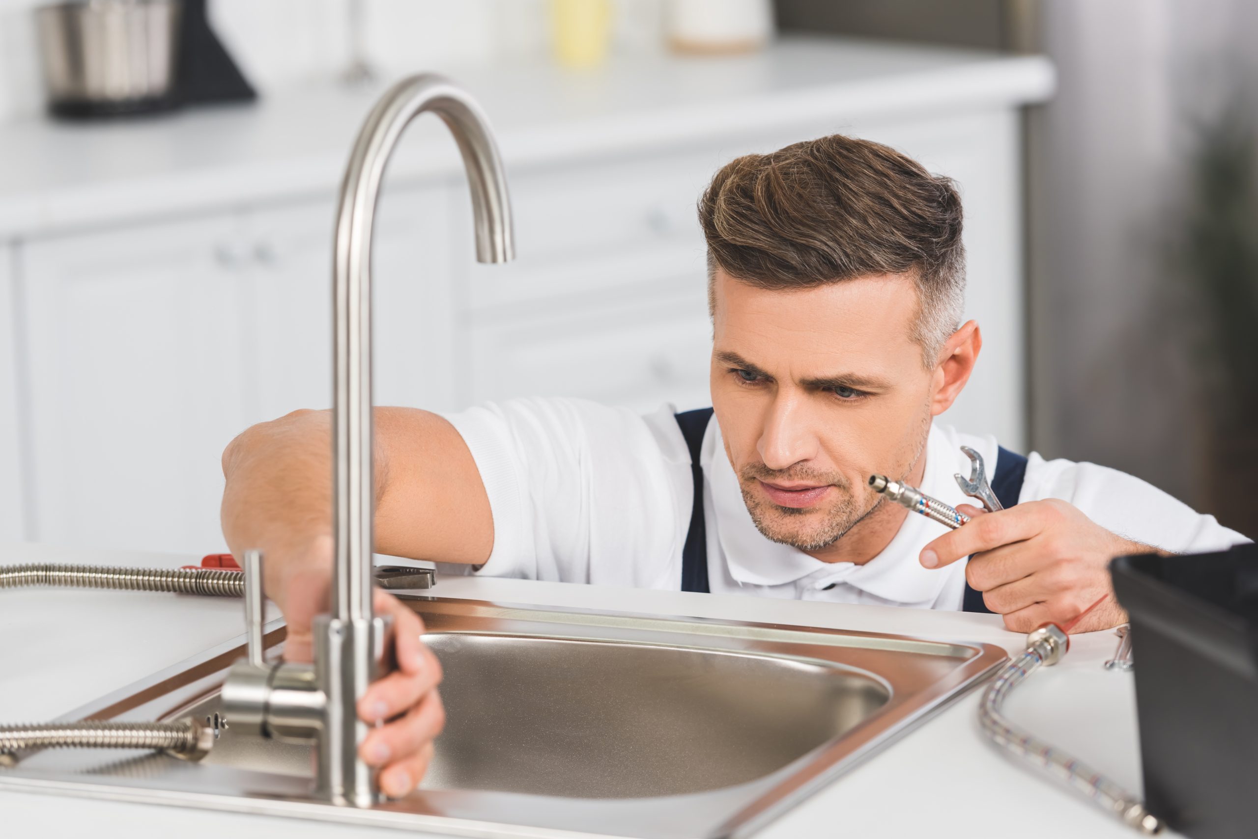 adult repairman holding pipe and spanner while repairing faucet at kitchen